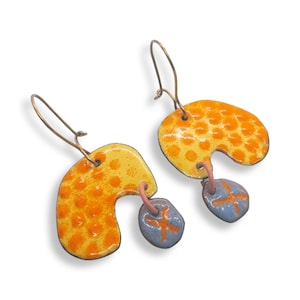 May include: A pair of yellow and orange enamel earrings with a blue and orange enamel dangle. The earrings are shaped like a crescent moon and have a textured surface.