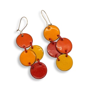May include: A pair of dangle earrings featuring multiple round discs in shades of orange, red, and yellow. The discs are connected by small red loops.
