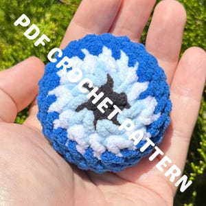 May include: A round, textured crochet item featuring a central black star shape surrounded by concentric layers of light blue, white, and dark blue yarn. The text PDF CROCHET PATTERN is overlaid across the center of the circular object.