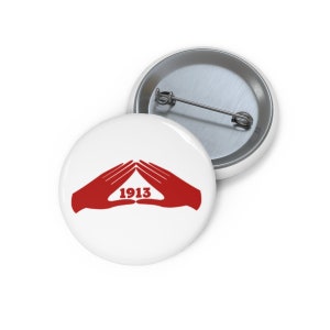 May include: White button with a red hand symbol forming a triangle with the year 1913 inside.