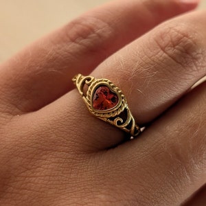 May include: A gold ring with a heart-shaped red gemstone set in a filigree design.