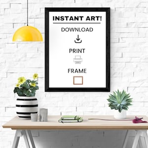 May include: A framed print with the text "INSTANT ART!" and instructions to download, print, and frame. The black frame is on a white brick wall. A yellow pendant light hangs above a wooden desk with plants and decor.
