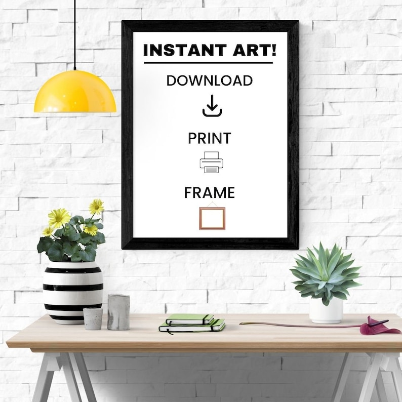 May include: A framed print with the text "INSTANT ART!" and instructions to download, print, and frame. The black frame is on a white brick wall. A yellow pendant light hangs above a wooden desk with plants and decor.