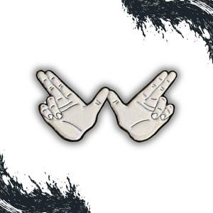 May include: A white enamel pin shaped like two hands forming the letter "W".