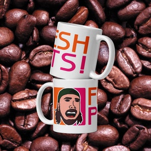 May include: Two white ceramic mugs stacked on top of each other. The top mug has the text "FRESH" in orange and "DOUGHNUTS!" in pink. The bottom mug has a cartoon illustration of a person with a green hat and the text "FRESH" in orange and "DOUGHNUTS" in pink.