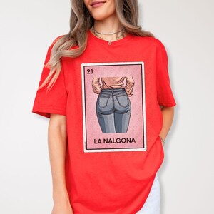 Op de afbeelding: Rood T-shirt met een afbeelding van een speelkaart met een vrouw in een blauwe jeans. De kaart is getiteld "21" en "La Nalgona".