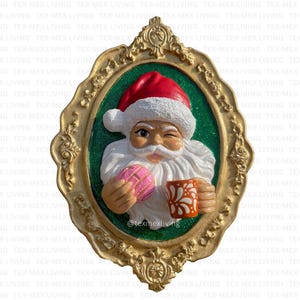 May include: A decorative wall hanging featuring Santa Claus winking, holding a pink pastry and a mug. The Santa figure is set against a green background within a gold-colored ornate frame. The image has the text "@texmexliving".