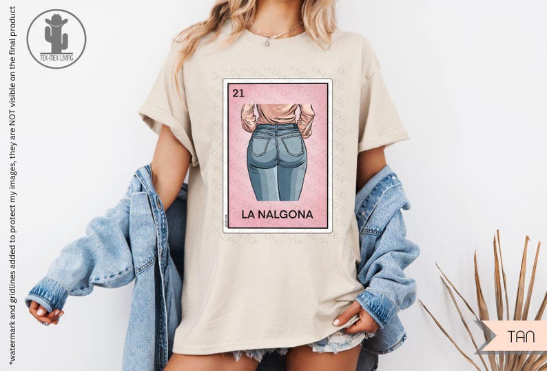 Op de afbeelding: Een beige T-shirt met een afbeelding van een roze kaart met het nummer 21 en de tekst "LA NALGO&Nu;&Alpha;". De kaart toont een cartoonillustratie van de rug van een vrouw die een blauwe jeans draagt.