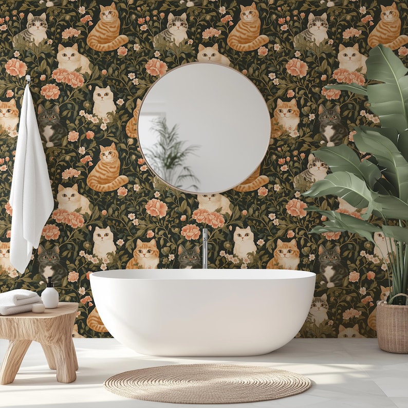 May include: A bathroom with a white oval bathtub, a round mirror, and a wooden stool. The wallpaper features a repeating pattern of cats and flowers in shades of orange, cream, and green. A white towel hangs on the wall, and a woven rug sits on the floor.