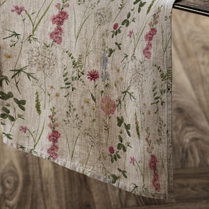 Peut inclure: Un chemin de table en lin beige avec un motif floral composé de fleurs sauvages roses, blanches et vertes. Le chemin de table a une texture subtile et une bordure frangée.