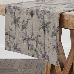 Op de afbeelding: Een beige tafelkleed met een grijze en paarse jungleprint met giraffen, olifanten en palmbomen.