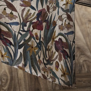 Könnte beinhalten: Ein beigefarbener Tischläufer aus Leinen mit einem floralen Muster aus blauen, grünen, gelben und roten Blumen. Die Blumen sind stilisiert und ähneln Iris, Orchideen und anderen exotischen Blüten.