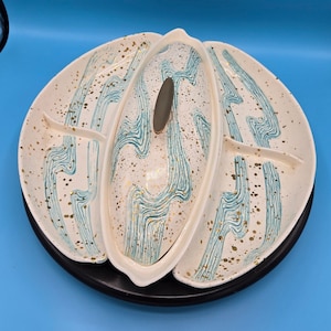 May include: A white ceramic serving dish with a blue and gold design. The dish has three sections and a separate lid. The lid has a blue and gold design and a small metal handle.