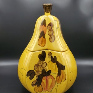 May include: Yellow ceramic pear-shaped cookie jar with a lid. The jar is decorated with brown and orange painted fruit and leaves. The lid has a brown stem-shaped handle.