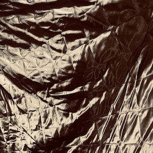 May include: Close-up of a brown quilted fabric with a satin sheen. The diamond pattern is created by stitching. The lighting creates shadows and highlights, emphasising the texture and sheen of the material.