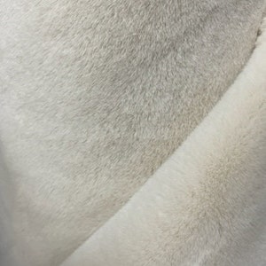 May include: Close-up of a soft, white faux fur fabric. The fabric has a fluffy texture and a subtle sheen.