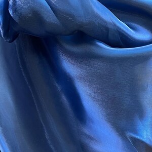 May include: Close-up of a deep blue fabric with a shiny, silky texture. The material is gathered and folded, creating shadows and highlights that emphasize its smooth surface. The fabric appears to be a flowing material.