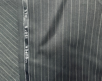 May include: Close-up of a dark gray fabric with thin white pinstripes. The fabric has a label that reads "SUPER 130'S ALL WOOL?"