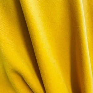 May include: A close-up of a bright yellow fabric with a soft, velvety texture. The fabric is folded and draped, creating a smooth, flowing surface.