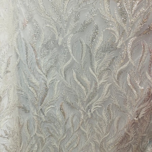 May include: White fabric with a silver glitter leaf pattern. The fabric is sheer and has a delicate texture.