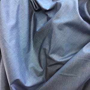 May include: A close-up shot of a crumpled, blue fabric. The fabric has a slight sheen and appears to be a lightweight material, with visible folds and creases. The color is a medium shade of blue, with subtle variations in tone due to the folds.