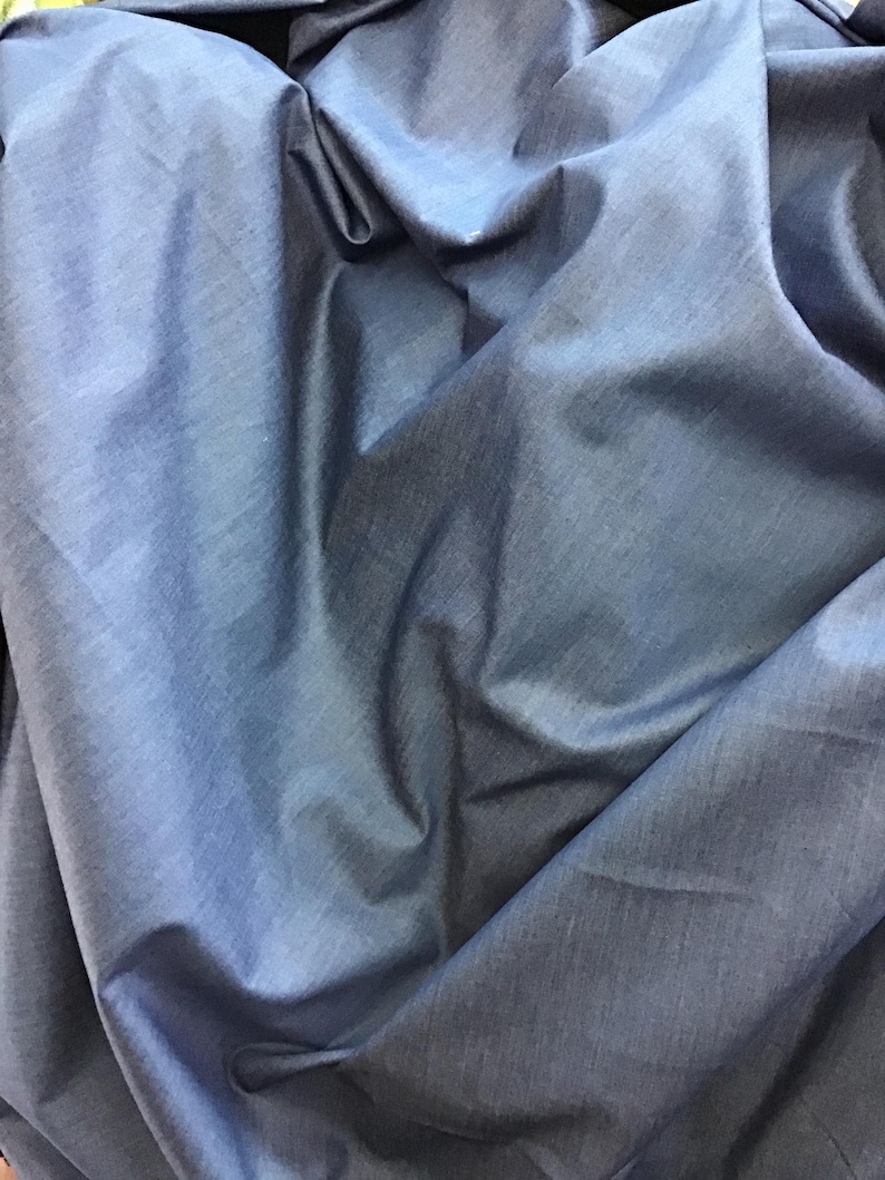 May include: A close-up shot of a crumpled, blue fabric. The fabric has a slight sheen and appears to be a lightweight material, with visible folds and creases. The color is a medium shade of blue, with subtle variations in tone due to the folds.