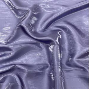 Peut inclure: Gros plan sur un tissu lavande avec un aspect brillant et satiné. Le matériau est drapé et plié, créant des ombres et des reflets qui mettent en valeur sa texture. Le tissu semble lisse et fluide, suggérant qu'il est léger.