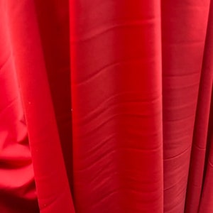May include: Close-up of a bright red fabric with a smooth, silky texture. The fabric has a subtle sheen and appears to be lightweight.
