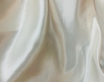 Puede incluir: Una tela de satén lisa de color blanco roto con un brillo sutil. La tela está drapeada y doblada, mostrando su textura lujosa.
