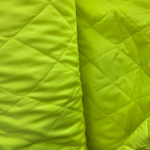 May include: Close-up of a bright yellow quilted fabric with a diamond pattern. The fabric is soft and smooth.