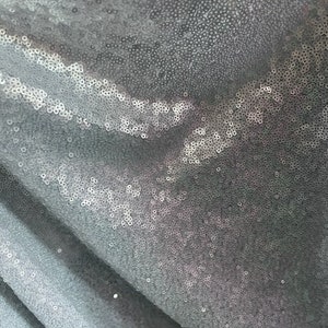 May include: A close-up of a silver sequined fabric. The sequins are small and tightly packed, creating a shimmering effect.