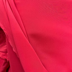 Pode incluir: Close-up de um tecido rosa vibrante com uma textura lisa e sedosa. O tecido está dobrado e drapeado, criando dobras e curvas suaves.