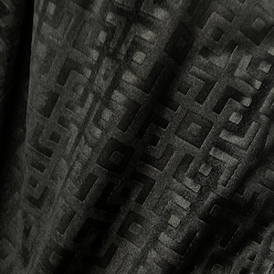 May include: Black fabric with a geometric pattern embossed into the surface. The pattern is made up of squares and rectangles.