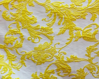 May include: White fabric with a yellow floral pattern. The pattern is a repeating design of stylised leaves and flowers.