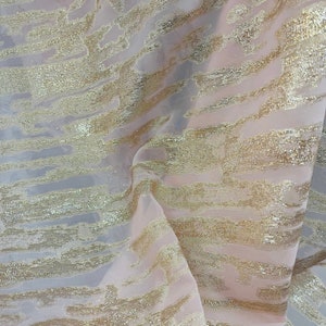 Puede incluir: Tela transparente rosa pálido con rayas doradas brillantes. La tela tiene un brillo sutil y una textura suave y delicada.