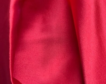 May include: Close-up of a smooth, bright red fabric. The fabric has a slight sheen and is folded in a way that creates a soft, flowing texture.