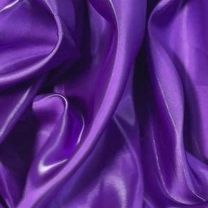 Peut inclure: Gros plan sur un tissu satiné violet vif. Le tissu est drapé et plié, créant des courbes et des ombres douces. Le satin a un éclat brillant, reflétant la lumière et ajoutant de la profondeur à l'image. L'effet général est luxueux et élégant.