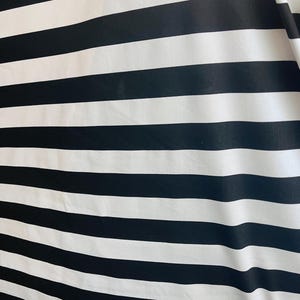 Könnte beinhalten: Ein Stoff mit breiten, horizontalen Streifen in Schwarz und Weiß. Die Streifen sind gleichmäßig breit und verlaufen über die gesamte Oberfläche. Der Stoff wirkt glatt und könnte für Kleidung oder Heimdekoration verwendet werden.