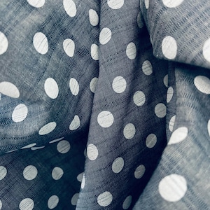 Puede incluir: Primer plano de una tela azul oscuro con un estampado de lunares blancos. La tela está doblada, creando sombras y resaltando la textura. Los lunares están espaciados uniformemente y varían ligeramente en tamaño.