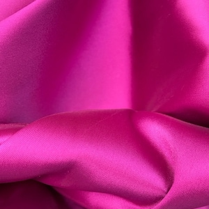 Peut inclure: Gros plan sur un tissu fuchsia vibrant avec une texture lisse et soyeuse. Le tissu est plié et drapé, mettant en valeur son toucher luxueux.