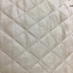 Puede incluir: Primer plano de una tela acolchada beige con un patrón de diamante. La tela tiene un brillo sutil y una superficie ligeramente texturizada.