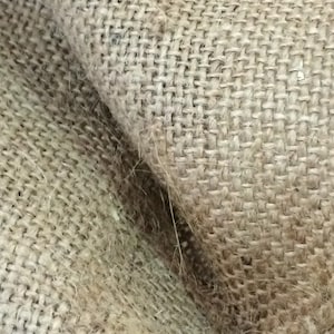 May include: Close-up of a brown burlap fabric with a woven texture. The fabric is folded over, showing the underside of the material.