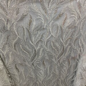 May include: White sparkly fabric with a delicate feather pattern. The fabric is sheer and has a subtle shimmer.