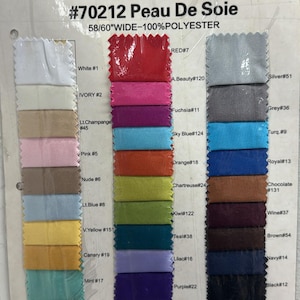 Pode incluir: Um cartão de amostra de tecido com várias cores de tecido Peau De Soie. O cartão exibe amostras retangulares em tons como branco, vermelho, rosa, azul e roxo. O texto no cartão diz "#70212 Peau De Soie 58/60" WIDE - 100% POLYESTER."