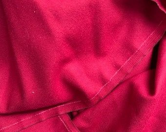 May include: Close-up of a vibrant pink fabric with a textured surface. The fabric is folded and stitched with white thread, creating a layered effect.
