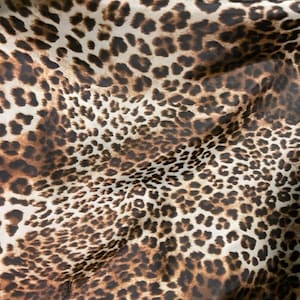 Puede incluir: Un primer plano de una tela de estampado de leopardo marrón y blanco. La tela tiene una textura suave y sedosa, ideal para proyectos de manualidades.