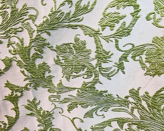 May include: A white fabric with an embossed green floral pattern. The pattern features intricate swirls and leaves.