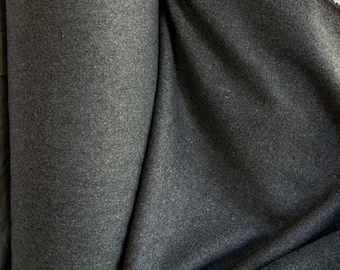 May include: A roll of dark grey fabric with a textured surface. The fabric is tightly rolled, with folds and shadows adding depth. The material appears to be a heavy weight, possibly wool or a wool blend.