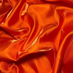 Peut inclure: Gros plan sur un tissu satiné orange vif avec des plis fluides et un éclat brillant. La texture du tissu crée des reflets et des ombres, ajoutant de la profondeur à l'image. La couleur est un orange vif et saturé.