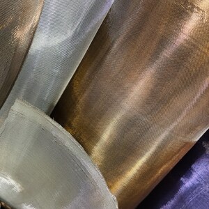 Könnte beinhalten: Nahaufnahme von mehreren Rollen schimmernden Stoffes in Gold-, Silber- und Lilatönen. Der Stoff hat eine feine Netzstruktur, die das Licht einfängt und einen glänzenden Effekt erzeugt. Ideal für Bastel-, Mode- oder Dekorationsprojekte.